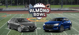 Two cars on a football field with the Almond Bowl log in between